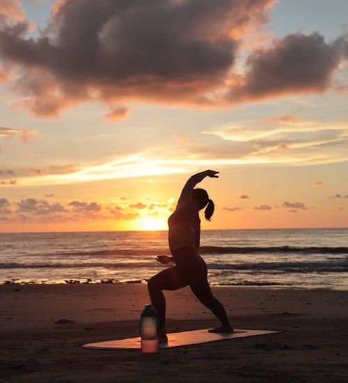 Person stretching peacefully during a beautiful sunrise outdoors.